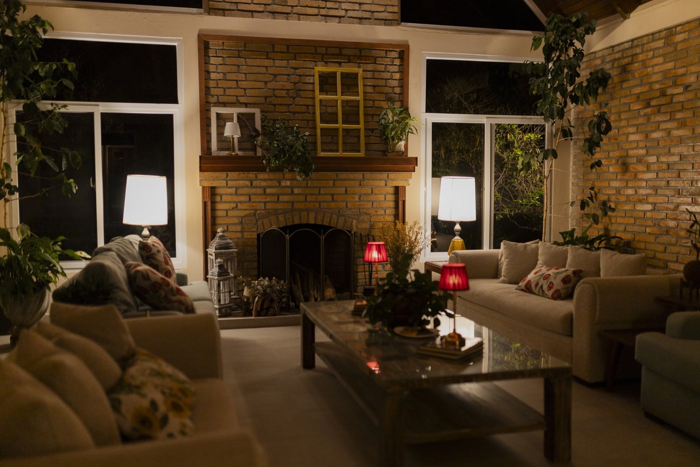 La sala entera de noche, con la chimenea de ladrillo y las lamparas encendidas