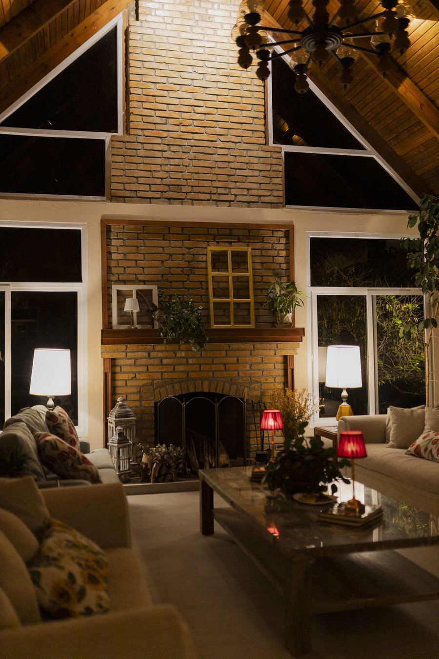 La sala de noche vista entera: la chimenea de ladrillo hasta el techo de dos aguas