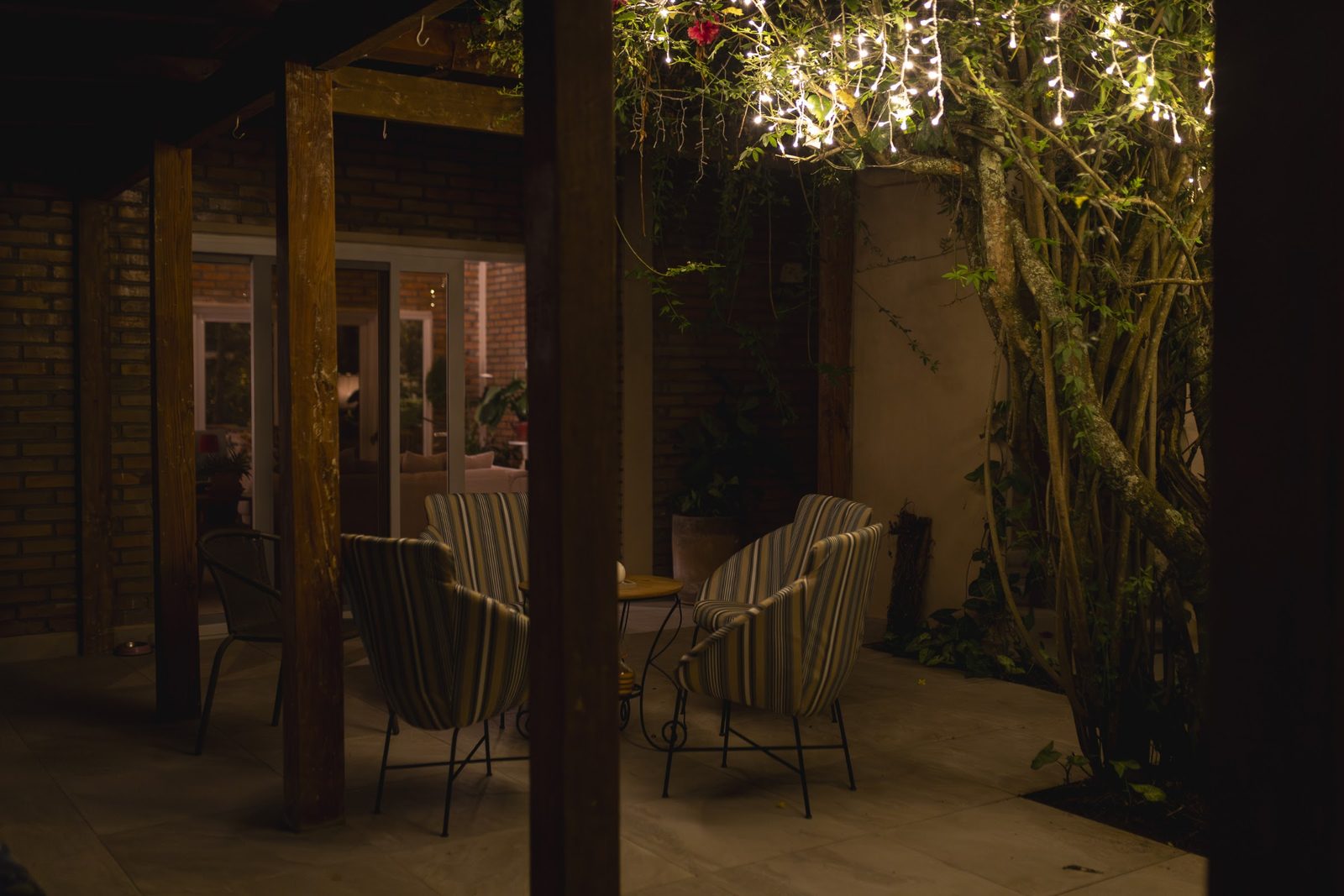 Sillas bajo el techo del patio y una enredadera con luces encendidas, de noche