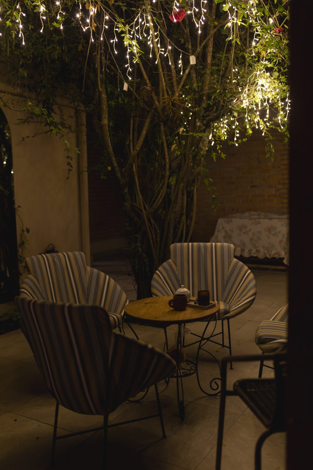 El patio de noche: sillas alrededor de mesas con lámparas, bajo una enredadera con luces