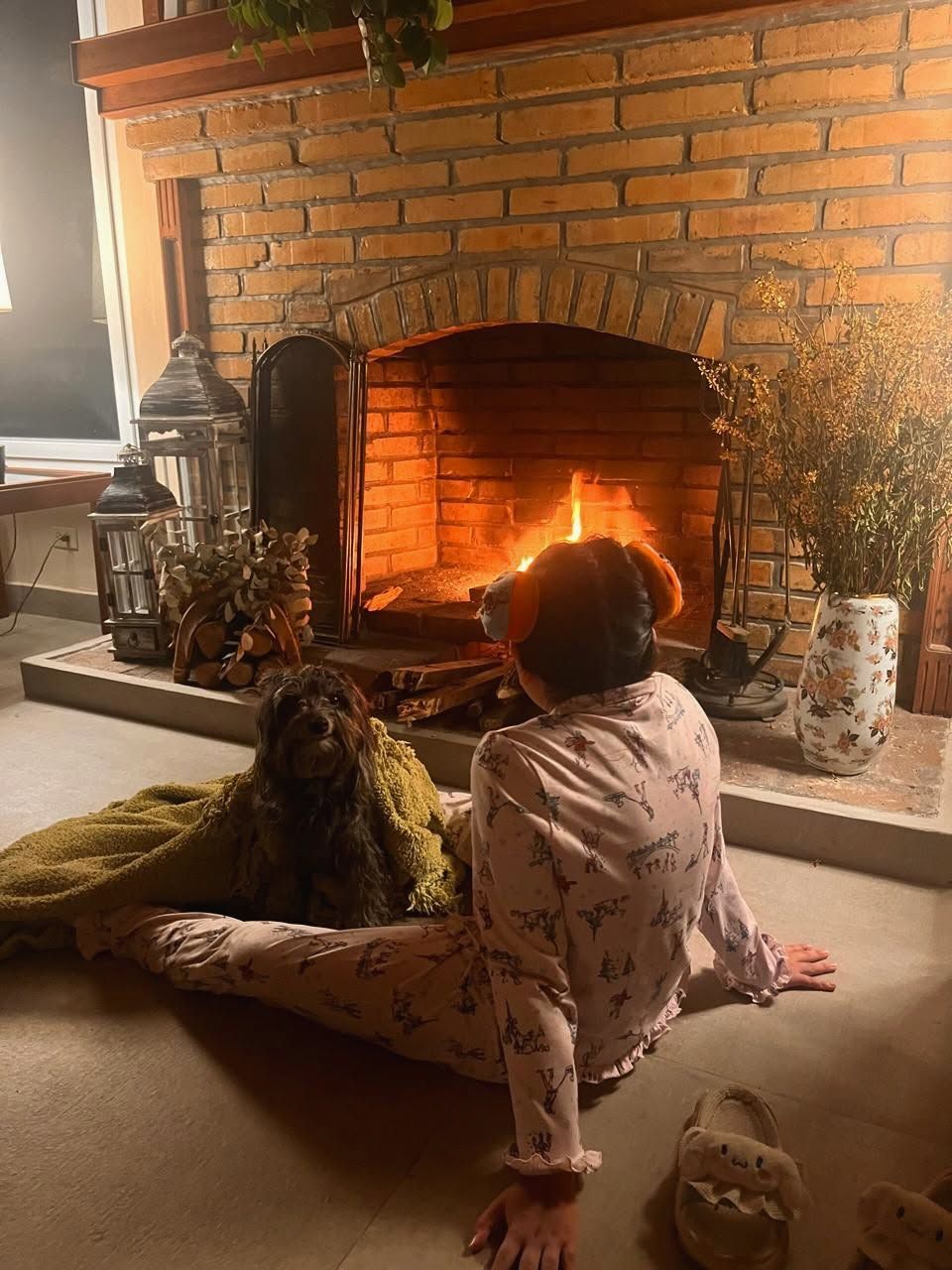 Una niña en pijama sentada frente a la chimenea encendida, junto a su perro