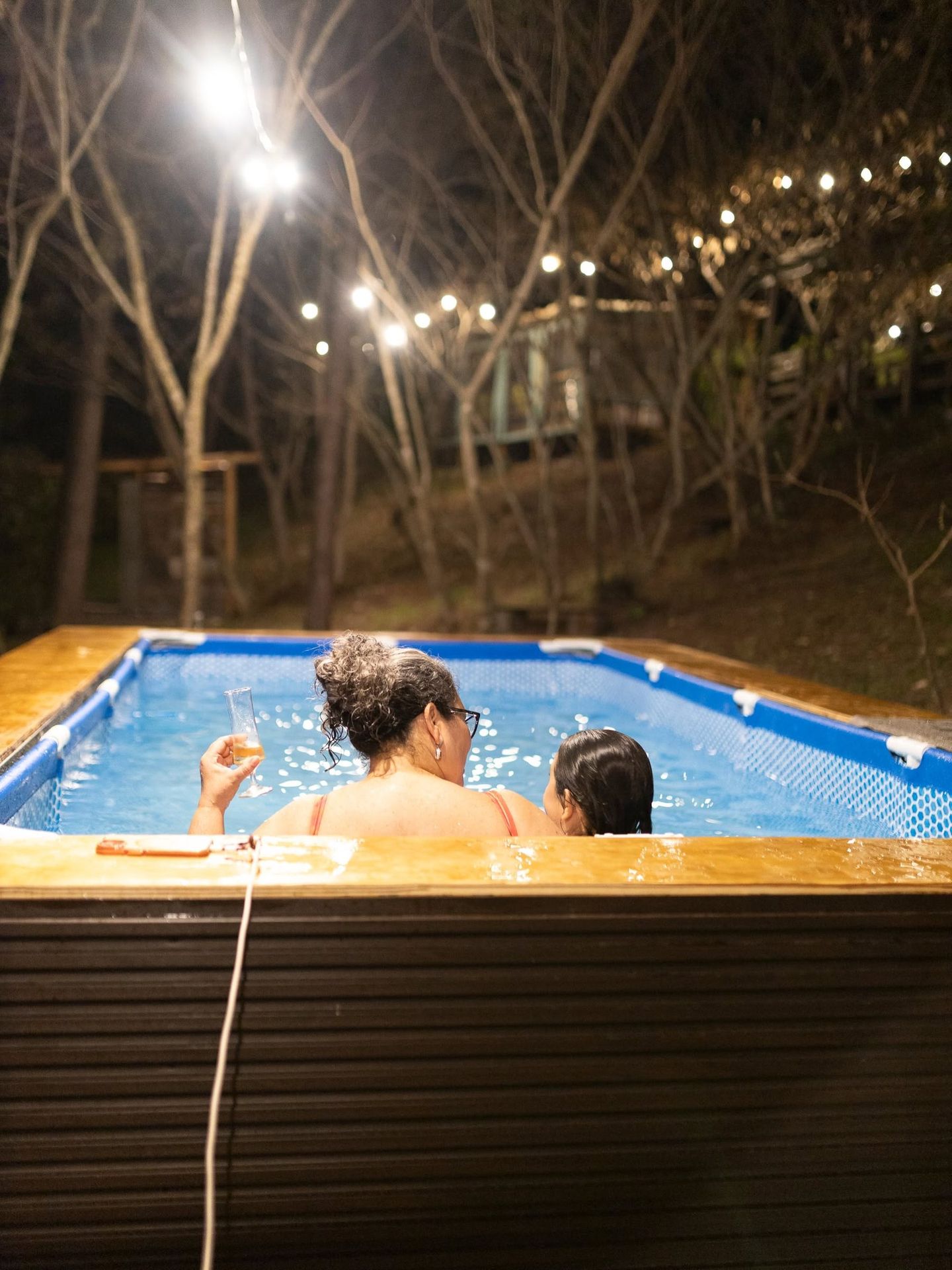 Dos personas en la piscina armable, de noche, bajo las luces colgadas