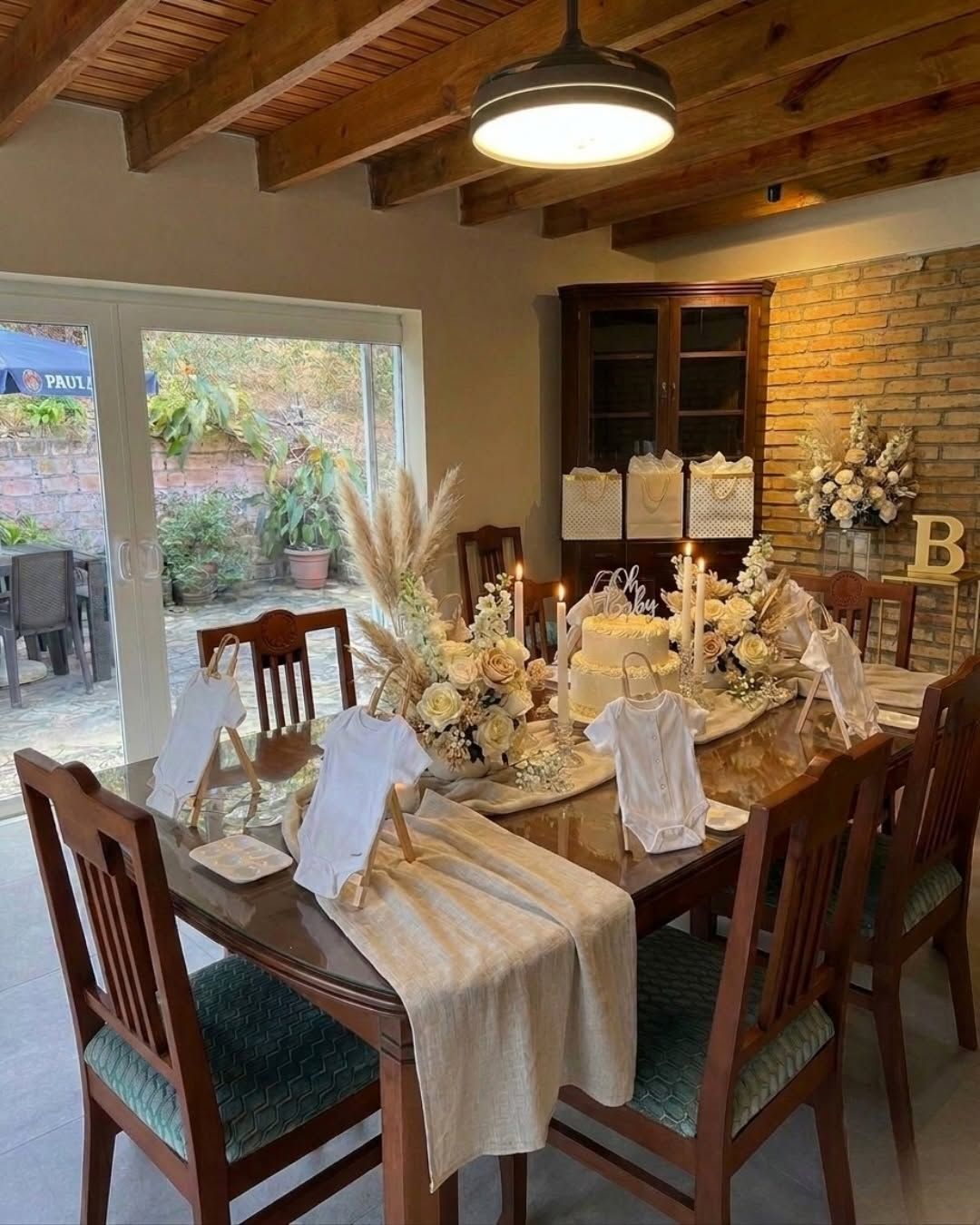 El comedor decorado con flores secas, ropa de bebé y un pastel blanco