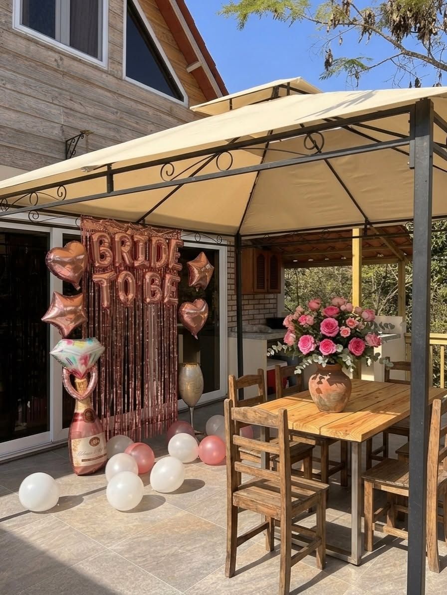 El gazebo del patio decorado con cortina rosada, globos y un ramo de rosas sobre la mesa