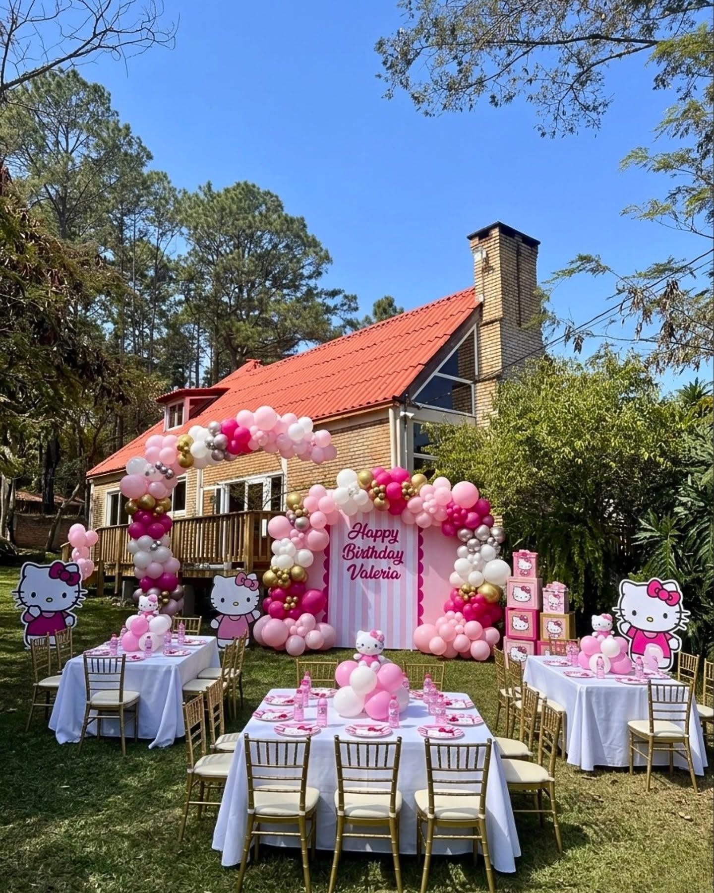 Cumpleaños infantil en el jardín: arco de globos rosados, mesas con mantel blanco y la casa al fondo