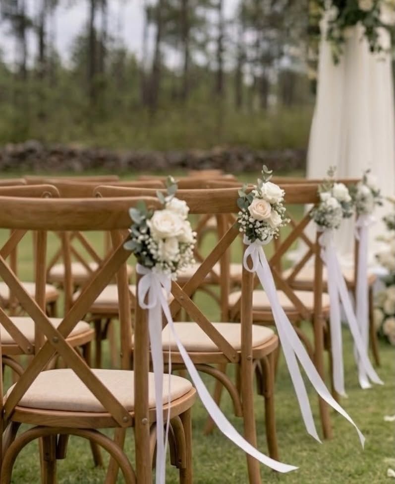 Sillas de madera con ramos de rosas blancas y cintas en el pasillo de la ceremonia
